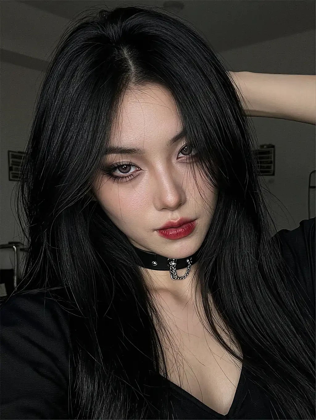 Fictional AI character with long black hair, red lipstick and a choker in a dark room